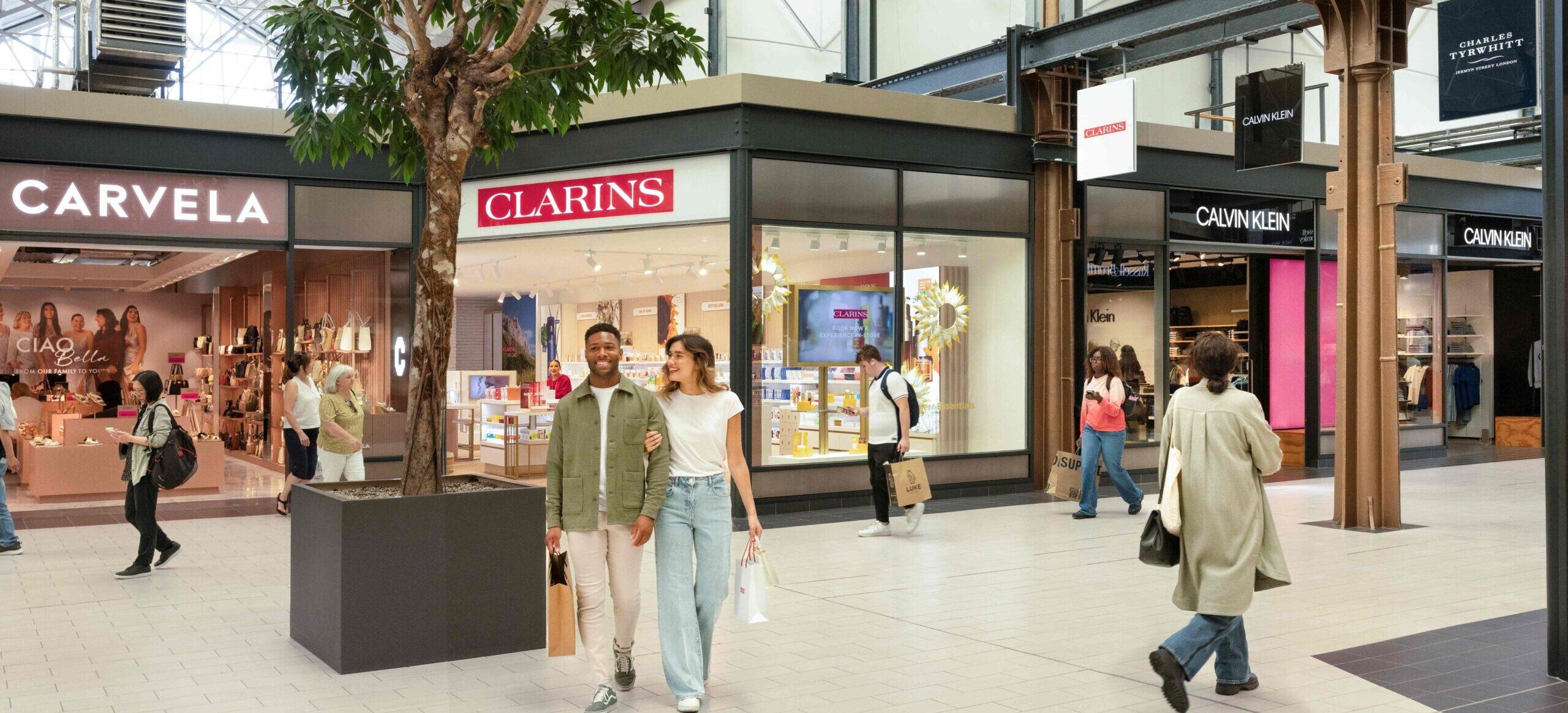 interior of designer outlet swindon with shoppers exploring the area. Clarins and Carvela can be seen. West mall.