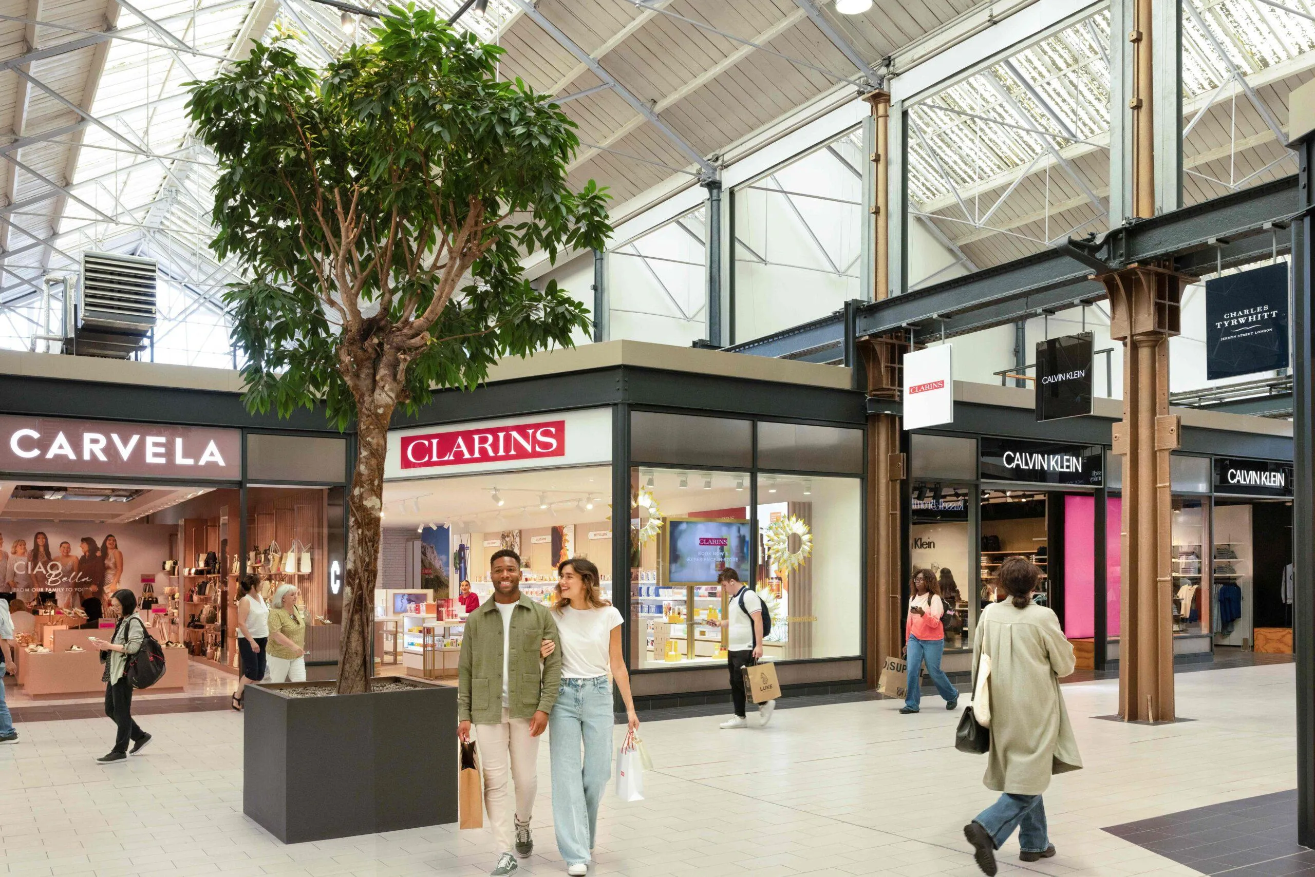 interior of designer outlet swindon with shoppers exploring the area. Clarins and Carvela can be seen. West mall.