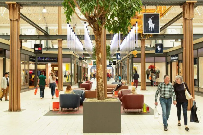 Polo west mall showcasing interior of designer outlet swindon. Shoppers seen walking around, with well-known brands such as tommy hilfiger and polo shown.